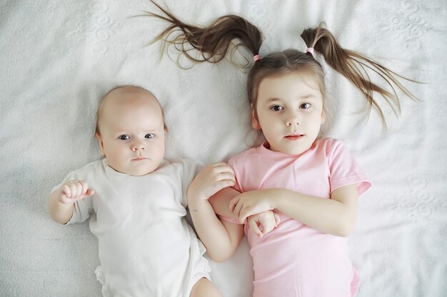 Los niños se acuestan en la cama junto al bebé recién nacido, hermanita. Emociones de los niños.