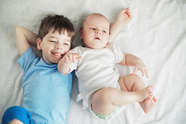 Los niños se acuestan en la cama junto al bebé recién nacido, hermanita. Emociones de los niños.