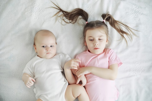 Los niños se acuestan en la cama junto al bebé recién nacido, hermanita. Emociones de los niños.