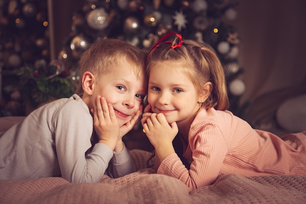 Los niños se acuestan en la cama y miran a la cámara. Adornos navideños, esperando las vacaciones.