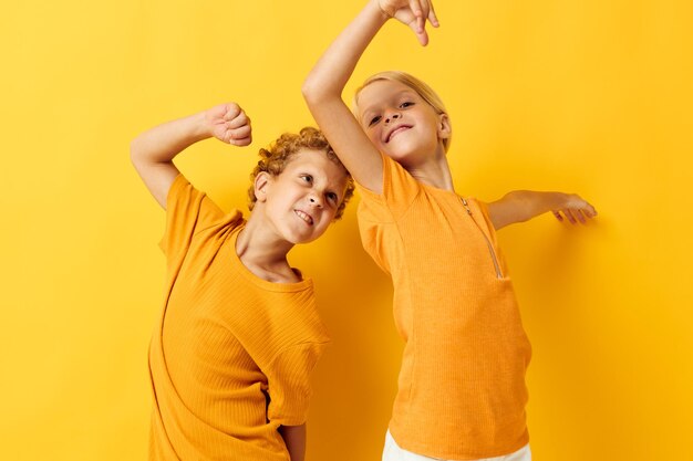 Niños alegres en camisetas amarillas de pie lado a lado emociones infantiles fondo amarillo inalterado