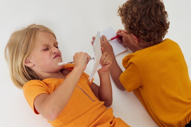 Niños alegres dibujando en cuadernos tirados en el suelo estilo de vida infantil inalterado