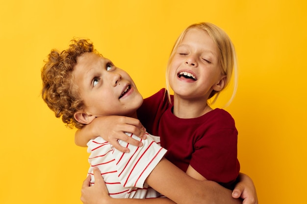 Niños alegres de pie uno al lado del otro posando emociones infantiles fondo amarillo