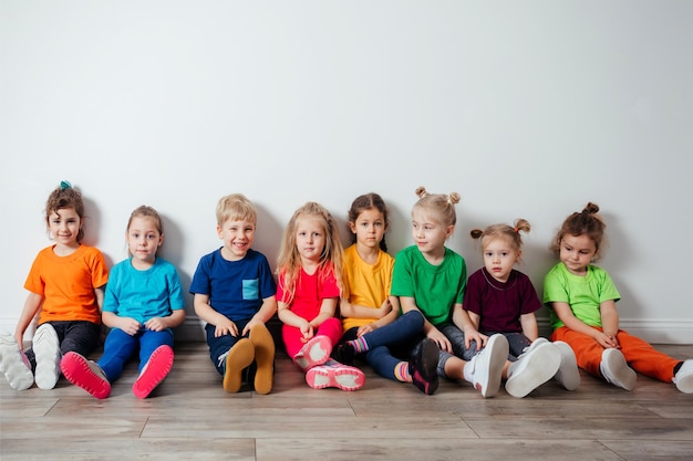 Niños alegres que se sientan en un piso cerca de la pared