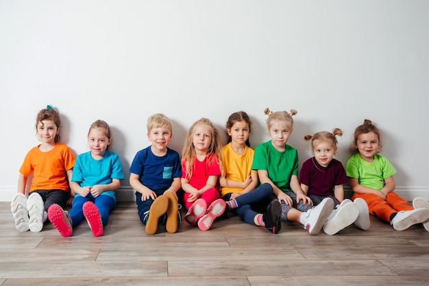 Niños alegres que se sientan en un piso cerca de la pared