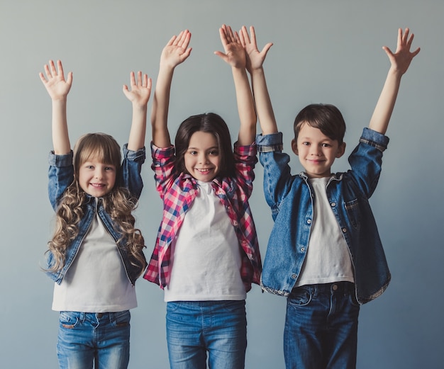 Niños alegres en ropa casual están levantando las manos.