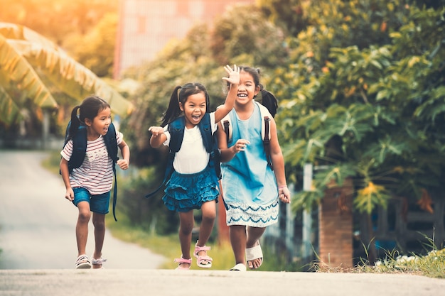 Niños de alumnos asiáticos con mochila corriendo e yendo a la escuela juntos