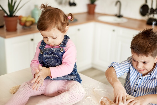 Los niños amasan la masa sentados en la mesa de la cocina.