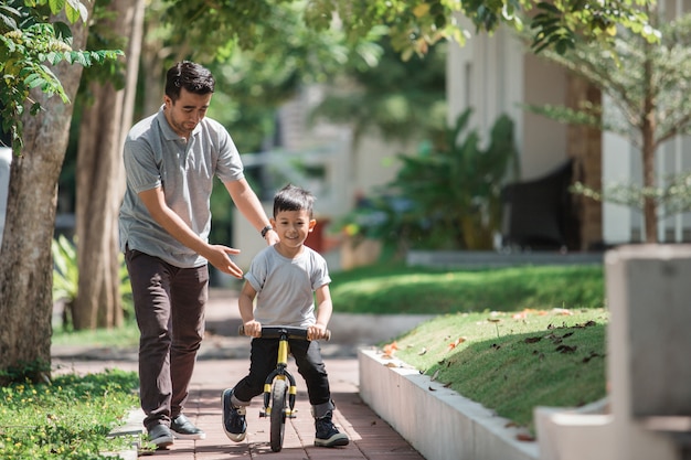 Los niños andan en bicicleta empujado por su padre