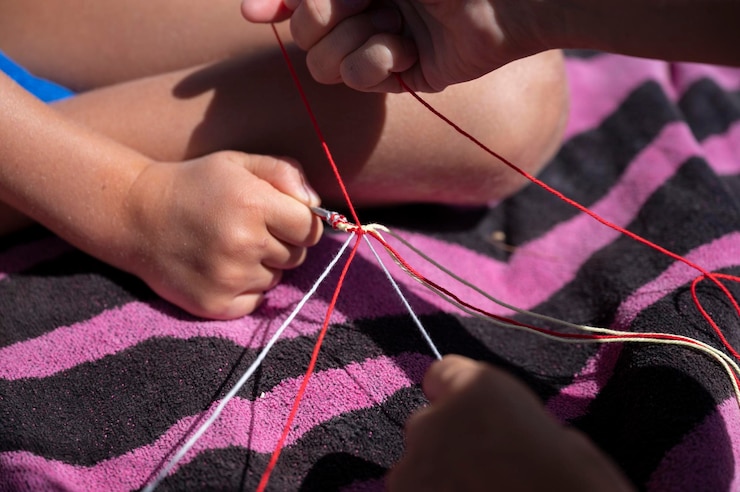Foto niños anudando hilos de algodón multicolor para hacer una pulsera