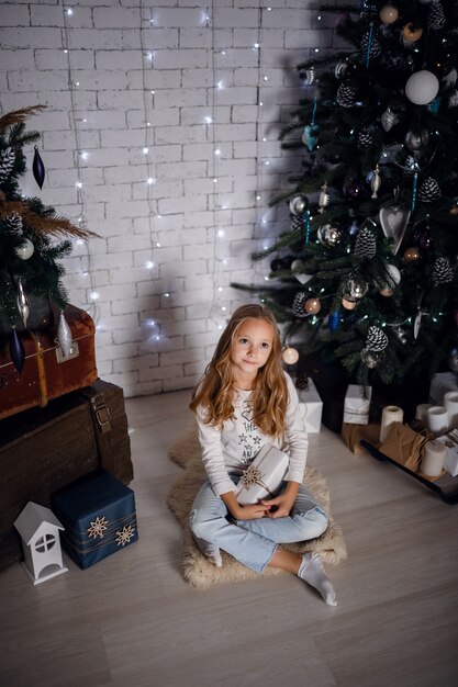 Niños bajo el árbol de Navidad con cajas de regalo. Decoraciones de año nuevo. estilo rústico, decoraciones de madera oscura. Interior de año nuevo. Hermanas.
