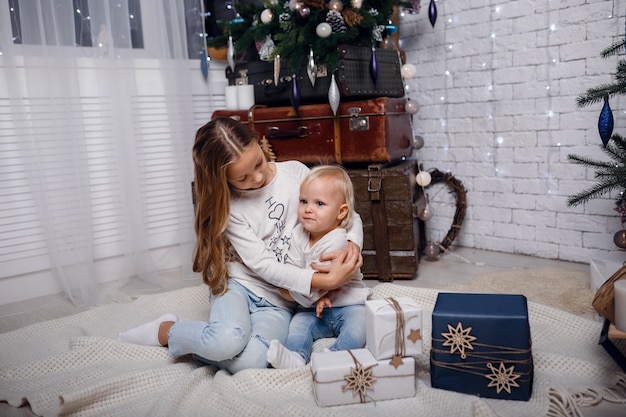 Niños bajo el árbol de Navidad con cajas de regalo. Decoraciones de año nuevo. estilo rústico, decoraciones de madera oscura. Interior de año nuevo. Hermanas.