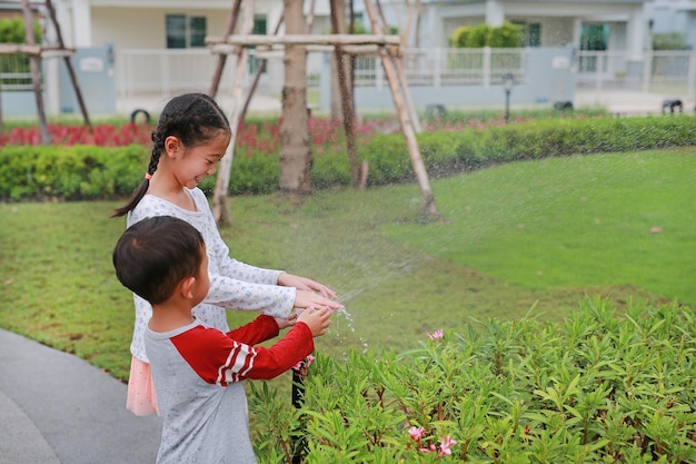 Niños asiáticos divirtiéndose para jugar al agua de regar las plantas.