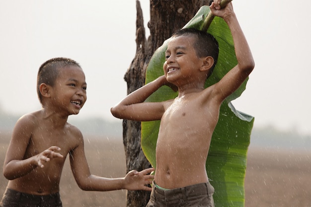 Los niños asiáticos están felices porque juegan bajo la lluvia. Después de una larga sequía