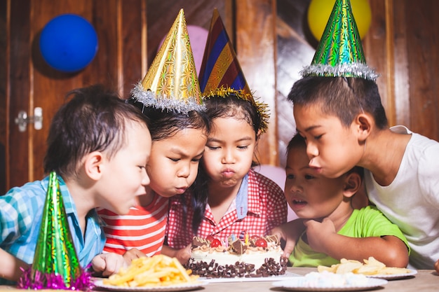 Niños asiáticos niñas y niños celebrando cumpleaños y soplando velas en un pastel de cumpleaños en la fiesta juntos