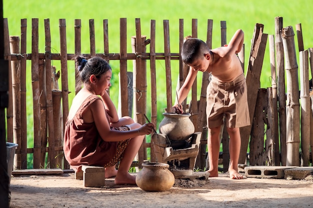 Niños asiáticos, un niño y una niña, están cocinando en la cocina de una casa de campo tailandesa, donde viven en el campo.