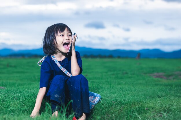 Los niños asiáticos con vestimenta local están usando un teléfono inteligente llamando a su madre para que la recoja en el campo después de terminar de pescar