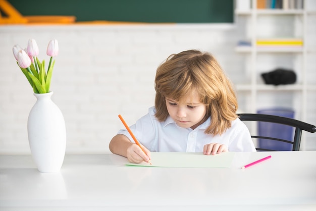 Niños en el aula de la escuela Niño de la escuela escribiendo en cuaderno y sentado a la mesa en el aula