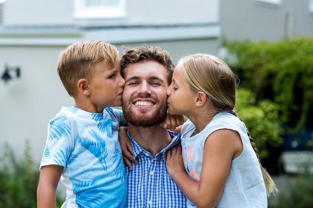 Niños besando a padre sonriente en el patio