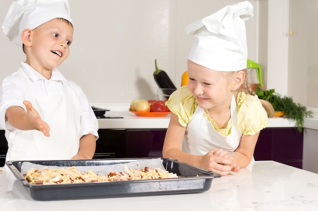 Niños blancos en delantal hicieron deliciosa pizza en la cocina