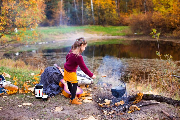 Los niños en el bosque de otoño en una parrilla de picnic salchichas y tocar la guitarra