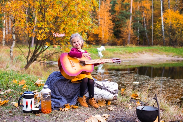 niños en el bosque de otoño en un picnic tocar la guitarra