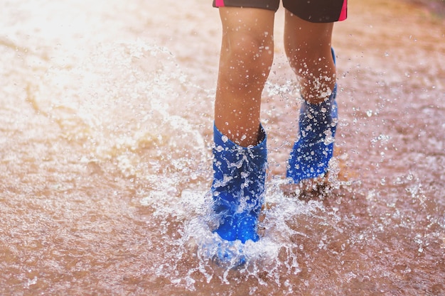 niños con botas de lluvia y saltando en charco en día lluvioso