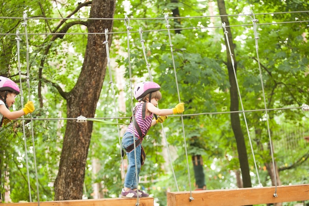 Niños en carrera de obstáculos en el parque de aventuras en casco de montaña y equipo de seguridad