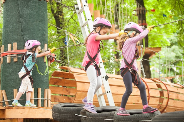 Niños en carrera de obstáculos en el parque de aventuras en casco de montaña y equipo de seguridad