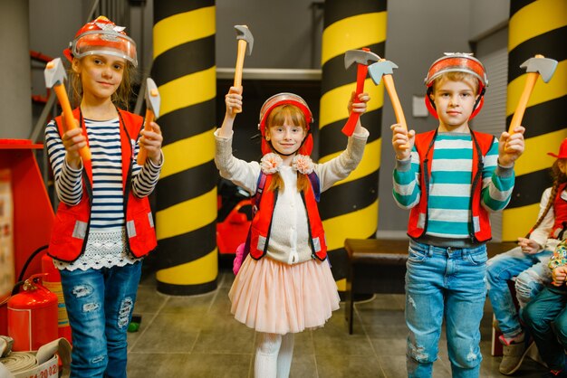 Niños con cascos y uniforme con herramientas en manos jugando a bombero