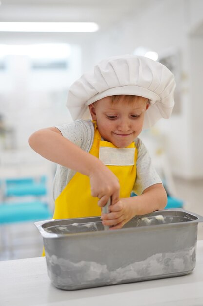 Los niños caucásicos con un delantal y un sombrero de chef amarillo hacen helado