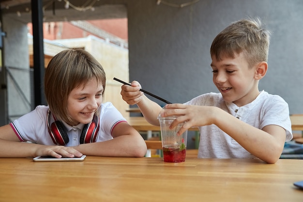 Los niños caucásicos sentados en el café jugando con bayas en una taza de limonada