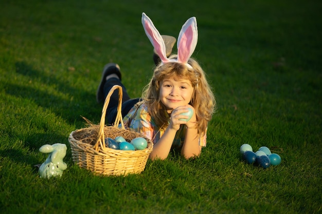 Niños cazando huevos de pascua en el parque tendido en la hierba lindo conejito niño con orejas de conejo