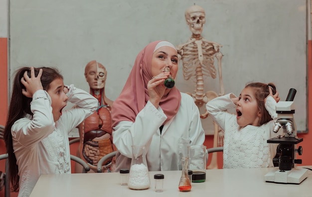 Niños científicos con una profesora musulmana haciendo divertidos experimentos de química en el laboratorio escolar