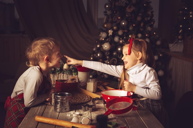 Los niños en la cocina juegan con harina. Adornos navideños, tradiciones familiares, comida navideña, vísperas de vacaciones.