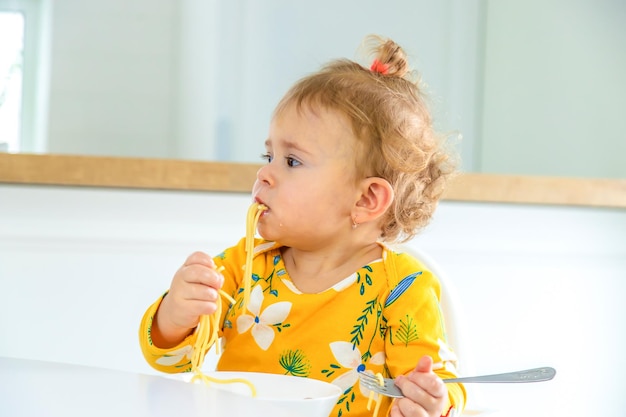 Los niños en la cocina en la mesa comen pasta.