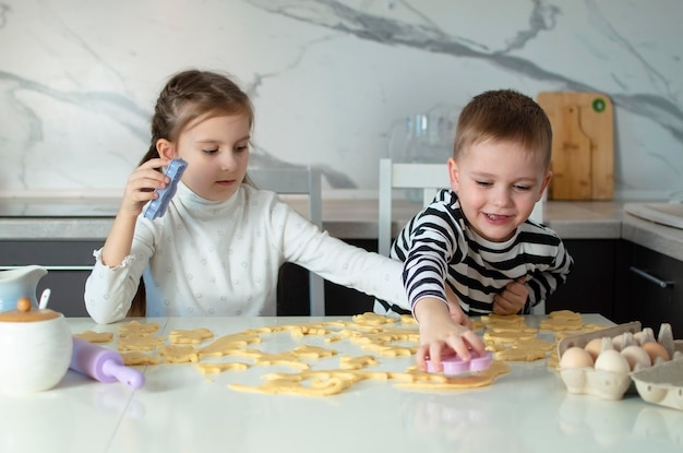 Los niños cocinan niños alegres hornean galletas en la cocina blanca a la niña le gusta cocinar en la cocina al niño feliz cocina la masa hornea galletes en la cocina los niños aprenden cosas nuevas