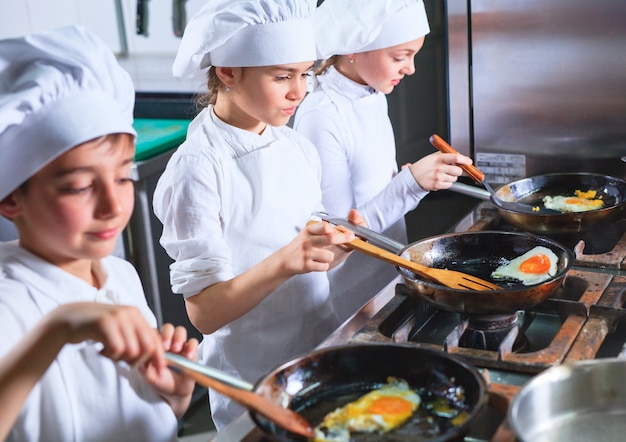 Niños cocinando el almuerzo en la cocina de un restaurante.