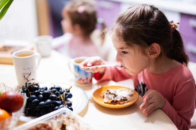 Los niños comen frutas y postres beben té en casa en la cocina nocturna.