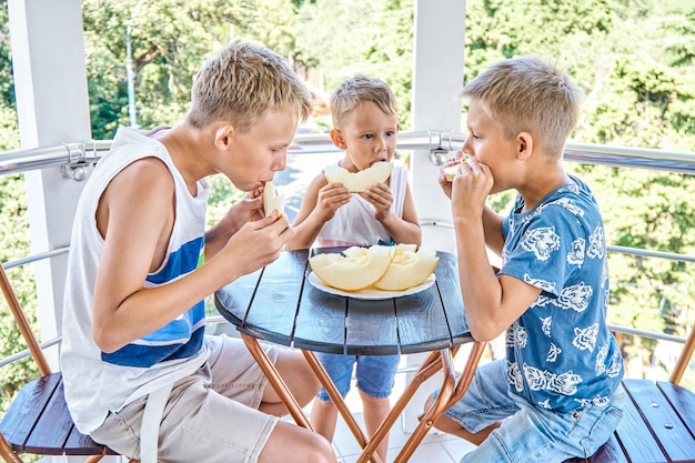 Los niños comen melón fresco en la terraza del hotel Los hermanos pasan juntos las vacaciones de verano en el balneario