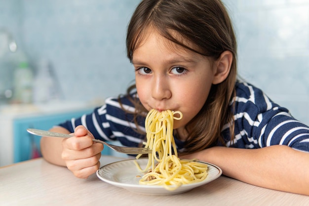 Los niños comen pasta. Almuerzo saludable para niños. Niño pequeño comiendo espaguetis a la boloñesa en una cocina azul en casa. El niño en edad preescolar prueba los fideos para la cena. Alimentos para la familia.