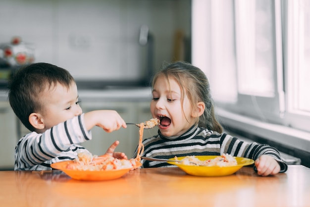 Los niños comen pasta en la cocina y se alimentan unos a otros