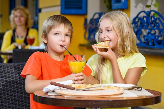 Los niños comen pizza y beben jugo al aire libre.