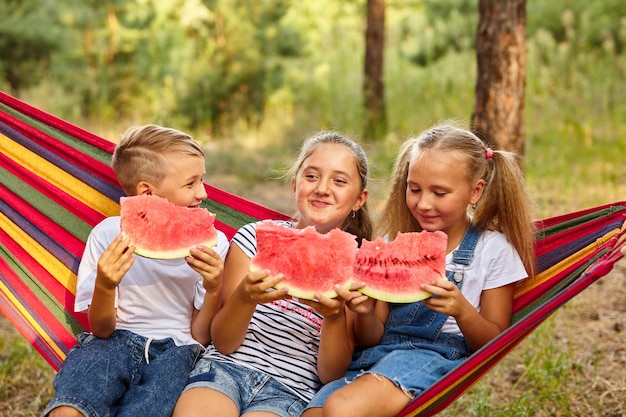 Los niños comen sandía y bromean al aire libre sentados en una hamaca colorida