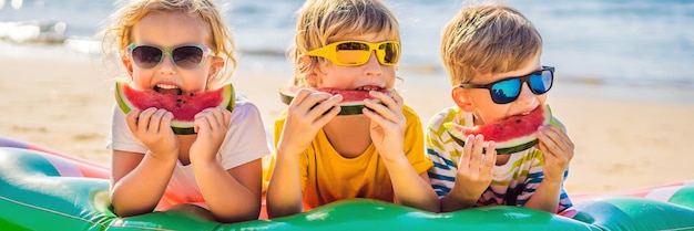 Los niños comen sandía en la playa con gafas de sol de formato largo