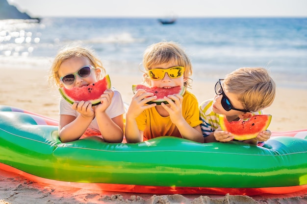 Los niños comen sandía en la playa con gafas de sol.