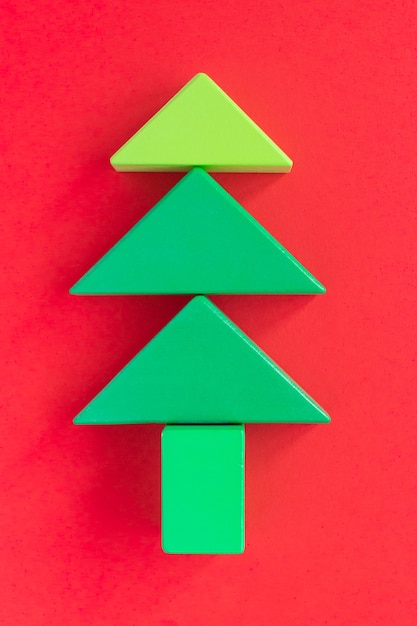 Niños de composición navideña. Árbol de Navidad hecho de bloques de construcción de madera verde sobre fondo rojo. Juguetes educativos coloridos para niños. Vista superior. Endecha plana.