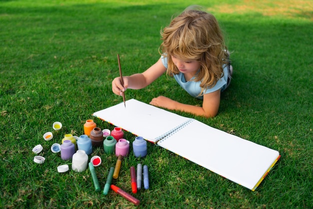 Los niños crean artista pinta creatividad vacaciones niño dibuja en el parque tendido en el césped divirtiéndose en na