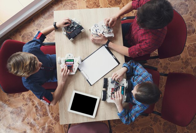 Niños creando robots en la escuela, vista superior, educación de tallo, espacio de copia. Desarrollo temprano, bricolaje, innovación, concepto de tecnología moderna.