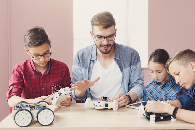 Niños creando robots con el maestro. El científico explica el nuevo material al grupo. Educación de tallo. Desarrollo temprano, educación, bricolaje, innovación, concepto de tecnología moderna